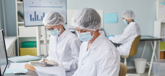 Personal de laboratorio con equipo de protección revisando documentos y datos como parte del control de pH en la industria alimentaria